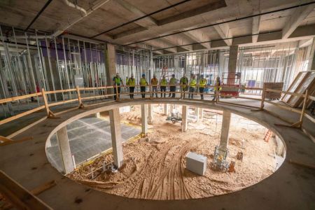 Construction workers and leaders gather around a gaping hole in the new Science and Health Sciences interior. The photo illustrates progress on the new building.