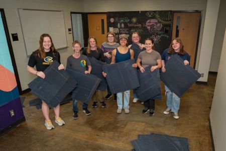 A group of students holds carpet tiles which they pried up from the floor to be recycled. 