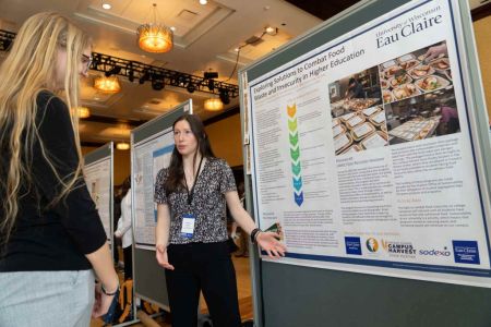 Student Kristen O'Brien explains her food recovery research poster to another person