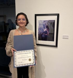 Bishop holds up scholarship in front of juried art show piece
