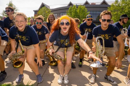 Members of the marching band cheer and pose for a photo with their instruments and matching t-shirts