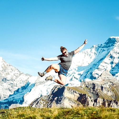 student jumping into the air in Sweden, snowy mountains behind 
