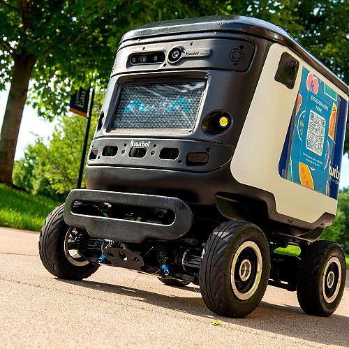A Kiwibot travels on a campus sidewalk.