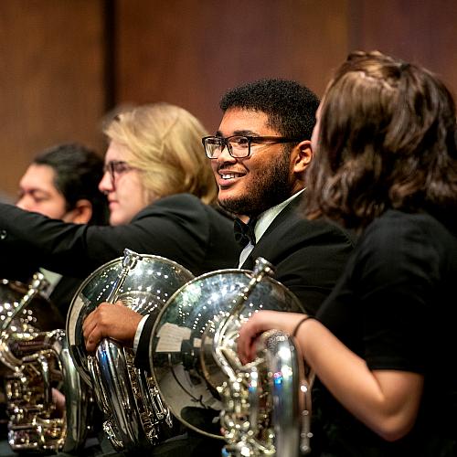 music students in horn section of orchestra during performance