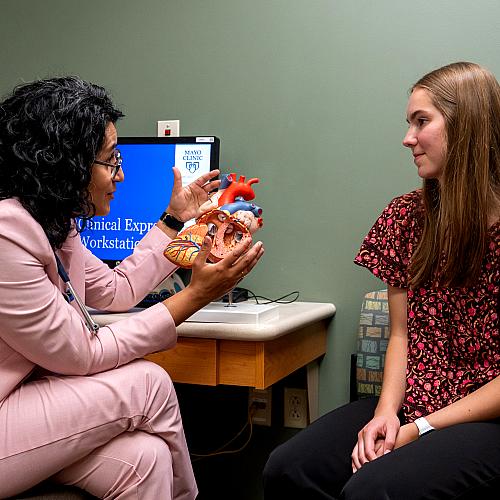 A student sits with a Mayo doctor in an exam room and looks at a 3D heart model.