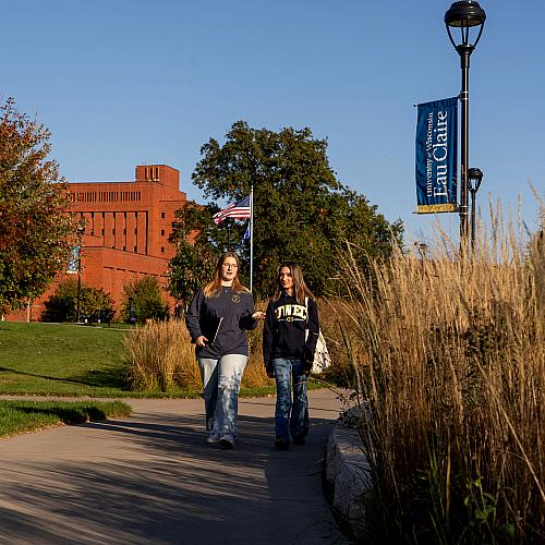 Two students walk across campus on a fall day