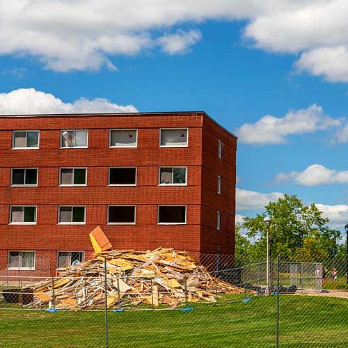A windowless brick dorm building has a pile of rubble in front of it from a demolition project
