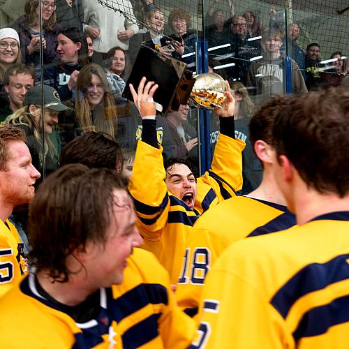 Hockey students celebrate their win while cheering and holding a trophy.