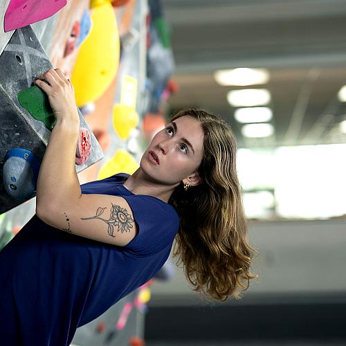 A student climbs a climbing wall looking determined.