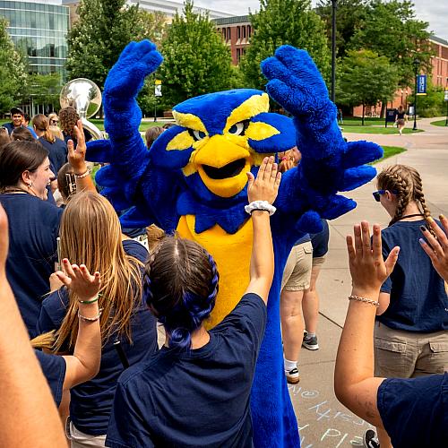 Blu celebrates the first day of school by putting their hands in the air alongside other students 