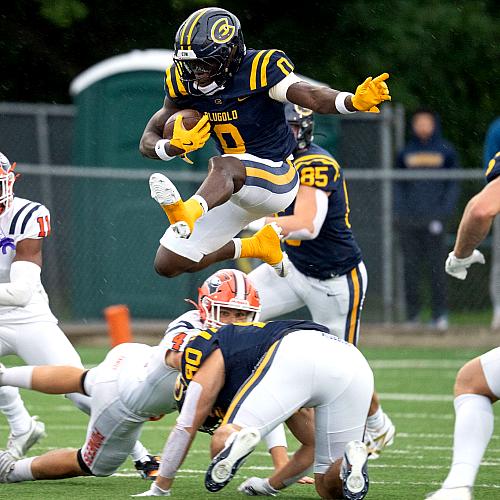 A Blugold football player hops over their opponent during the first football game of 2025.