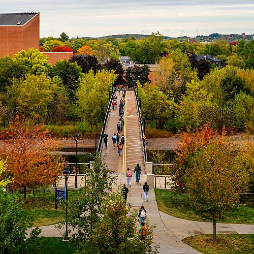 Students cross the bridge while fall colors surround them.