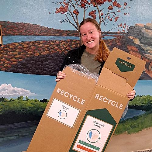 A student holds a new, unused cardboard nitrile recycle box in their hands 