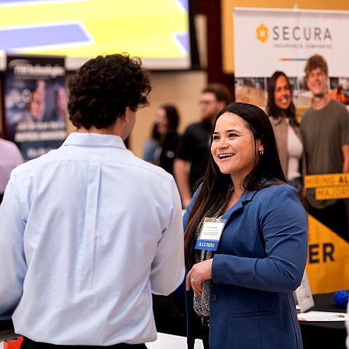 An alumni returns to interview Blugolds during a Career Fair. She shakes their hand and smiles.