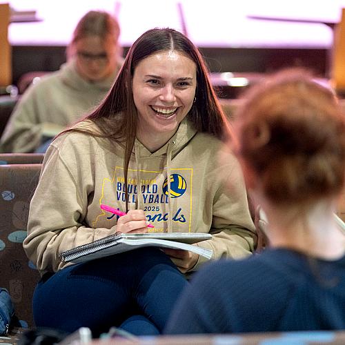 A student smiles brightly while taking notes.