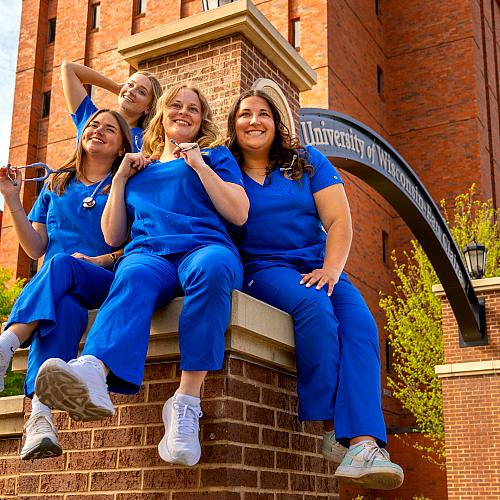 Nursing students sit atop the archway smiling in a more candid-looking shot.