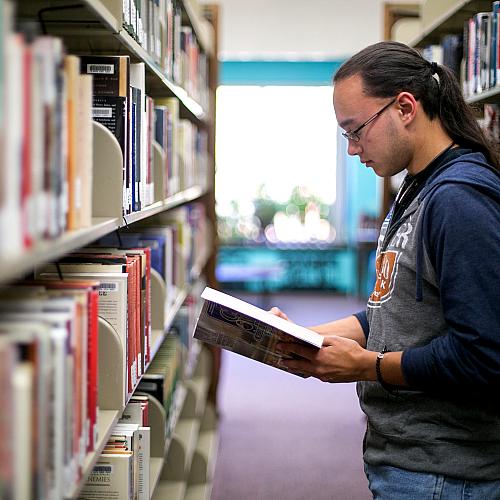 Male student in the library stacks looking at a book